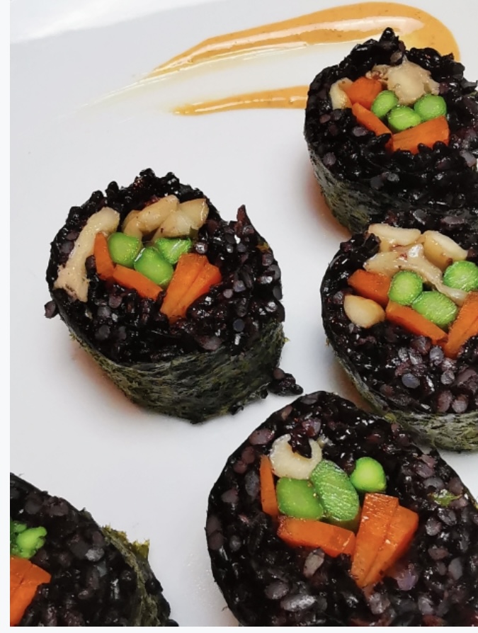 Black rice vegetable sushi rolls with carrot and edamame, plated with a swoosh of orange sauce