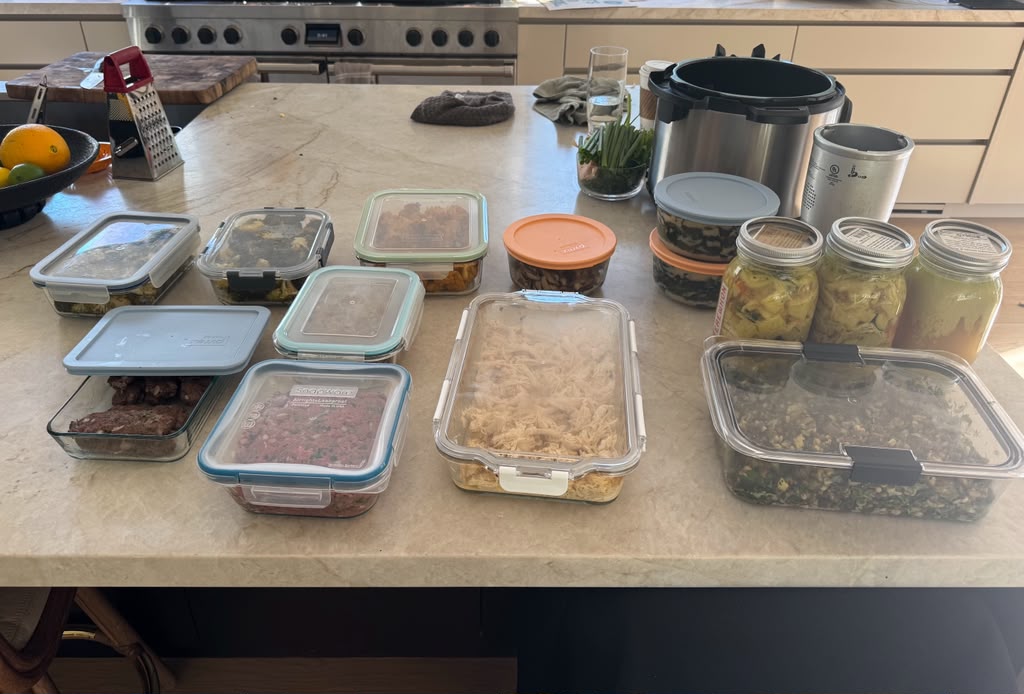 An assortment of weekly meal-prep containers and jars filled with prepared dishes on a kitchen island