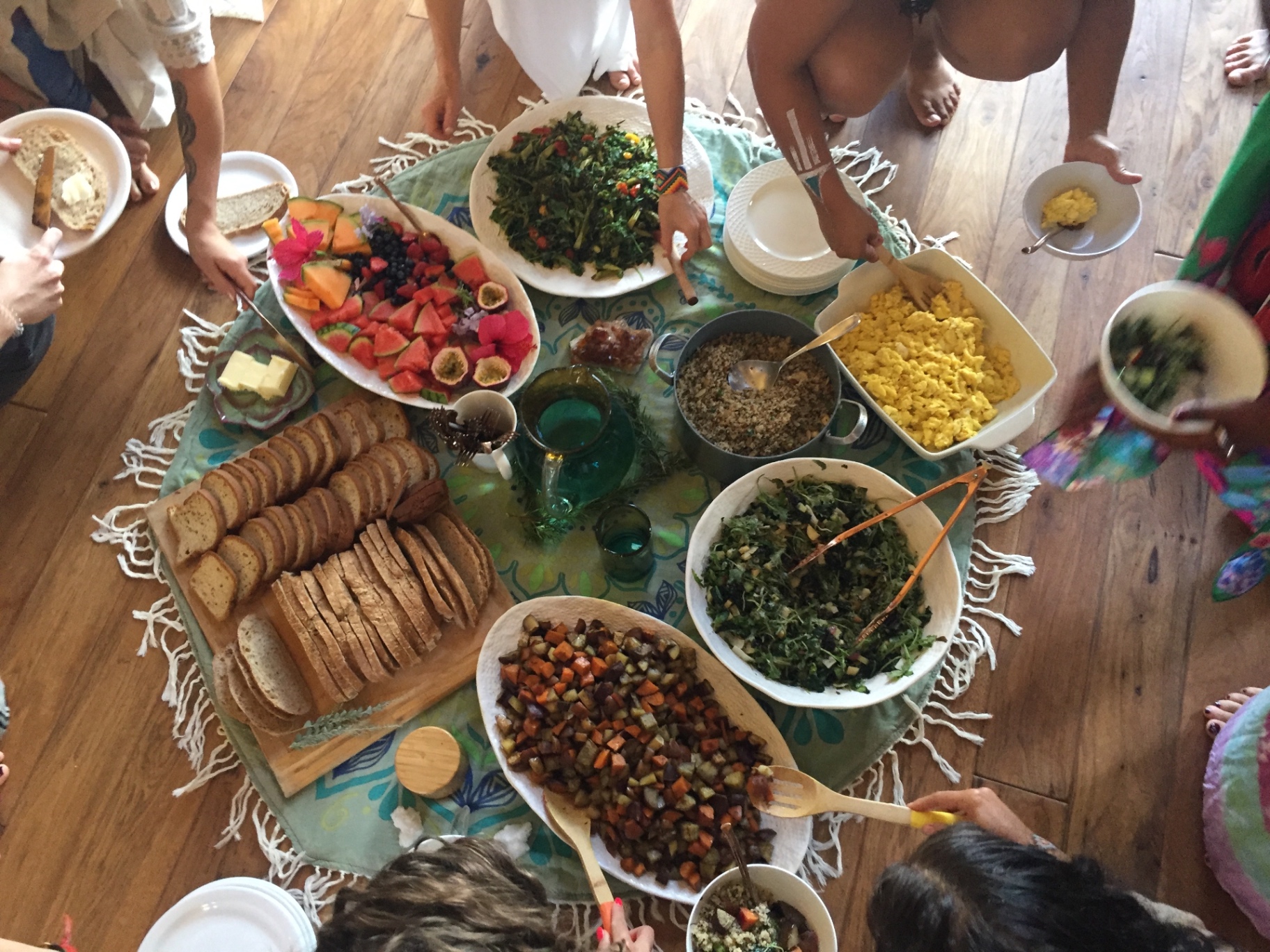 Overhead view of a colorful shared retreat meal with fresh fruit, breads, salads, and grains