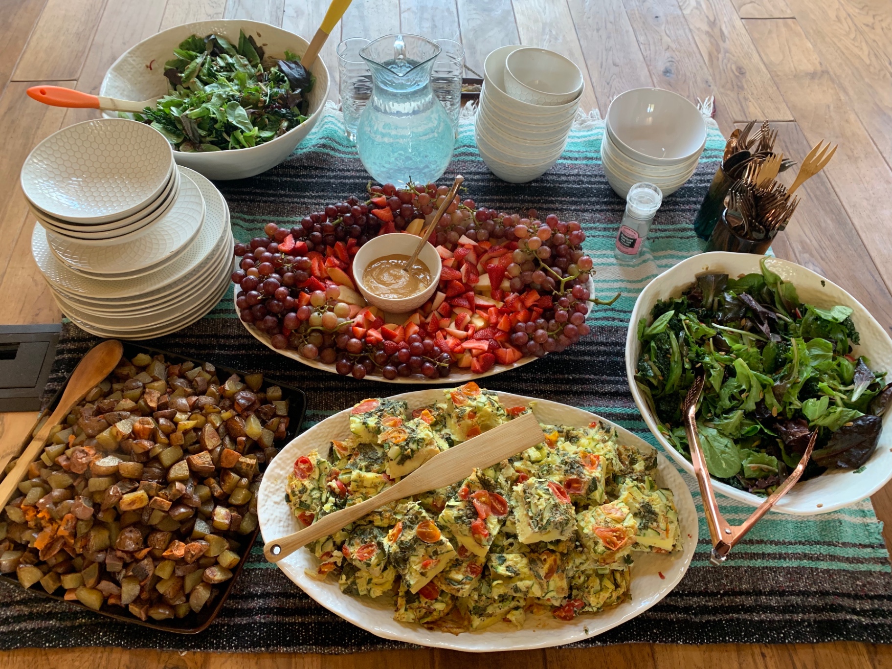 An overhead view of a retreat brunch spread with frittata, roasted potatoes, fresh fruit, and salads on a wooden table